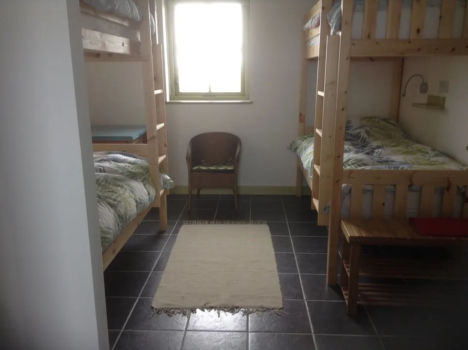 A bunk room with two timber bunk beds, a window between them, a wicker chair and a rug on the tiled floor