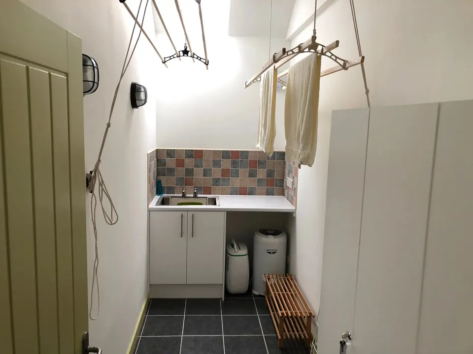 The drying room: a pulley rack hung with clothes above a utility sink and a slatted bench