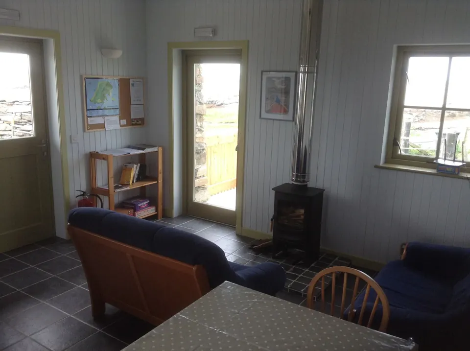 The wood-panelled living room with a leather sofa, a stove, and a glazed door opening onto the view
