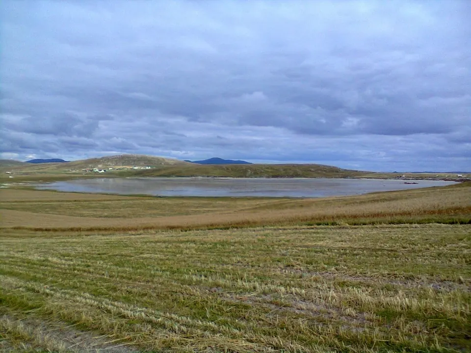 A loch reflecting a cloudy sky, seen across the machair