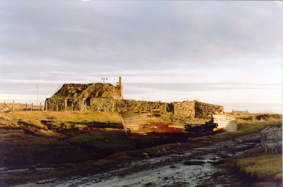 A ruined stone building and an old boat on the shore in low evening light