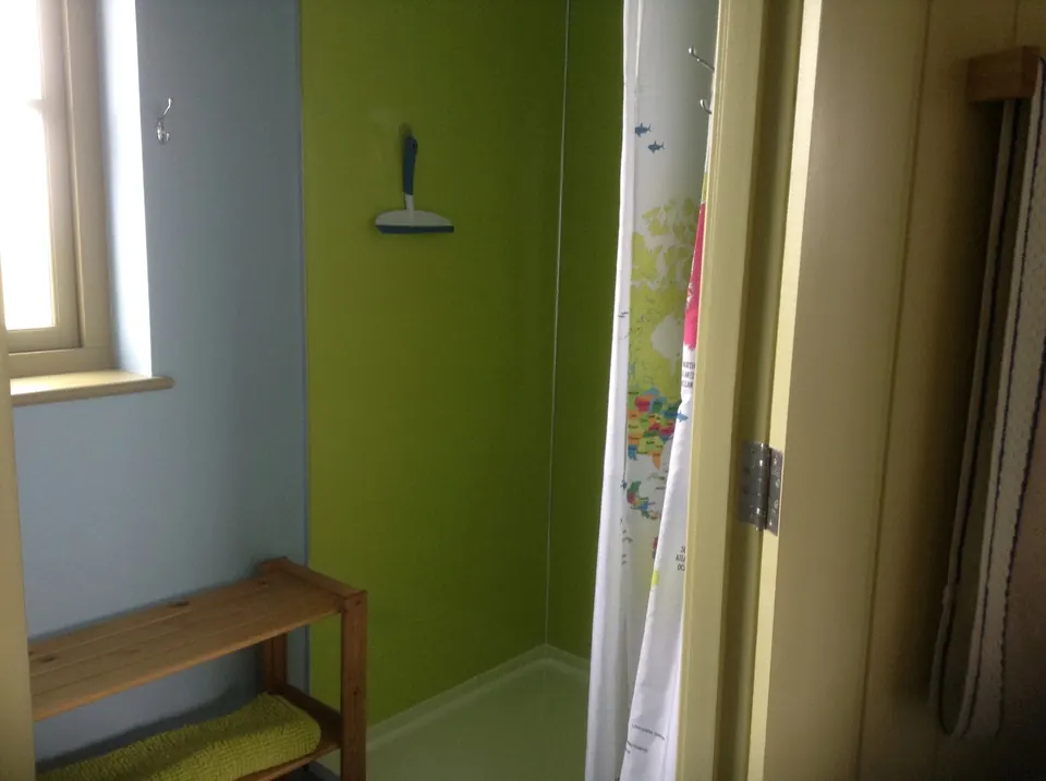 A shower room with a lime-green cubicle, a shower curtain and a wooden bench under the window